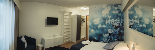 Un dormitorio con cama, televisor, armario y puerta de baño.