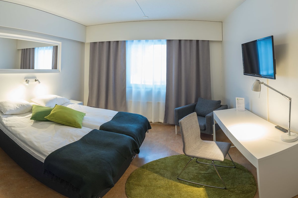 Ein Hotelzimmer mit einem Bett, einem Schreibtisch, einem Sessel, einem Fernseher und einem kleinen Tisch.