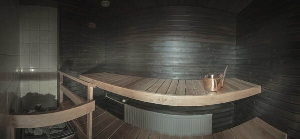 Un sauna avec un banc en bois et un seau en cuivre.