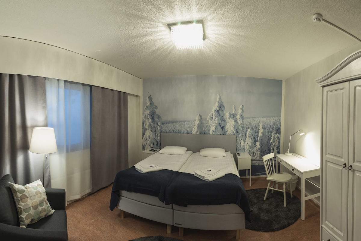Ein modernes Hotelzimmer mit Bett, Schreibtisch, Stuhl und Blick auf eine verschneite Landschaft durch das Fenster.