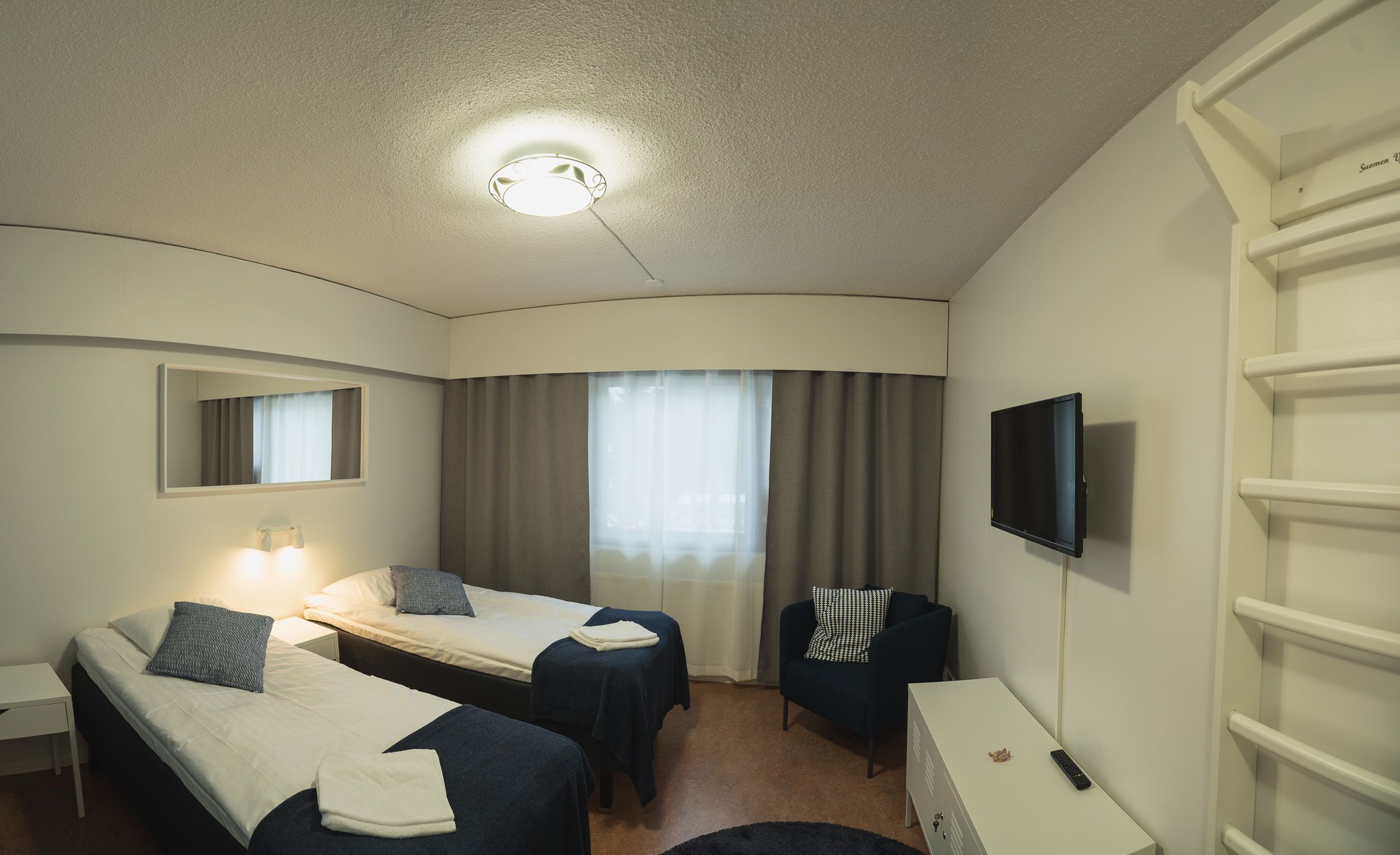 Une chambre d’hôtel avec deux lits, un bureau, une chaise, une télévision et une fenêtre avec des rideaux.