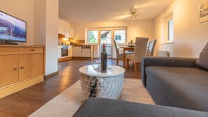 Ein modernes Wohnzimmer mit einem grauen Sofa, einem runden Couchtisch und einem Fernseher auf einer Holzkommode.