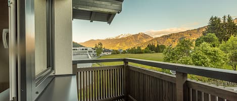 A wooden balcony with a view of a mountain range and a building in the distance.