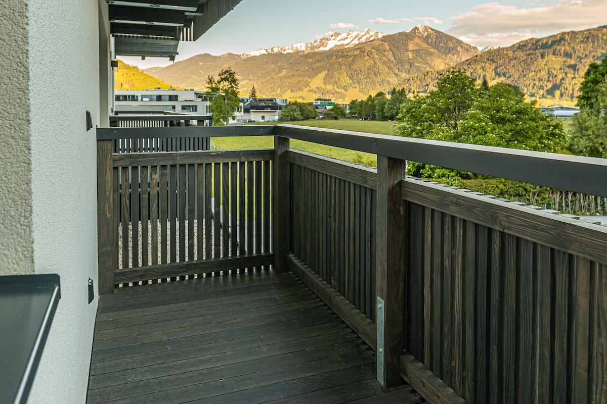 A wooden balcony with a metal railing overlooking a mountainous landscape.