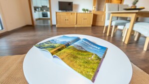Eine Zeitschrift liegt auf einem weißen Tisch in einem modernen Wohnzimmer mit einer Küche im Hintergrund.