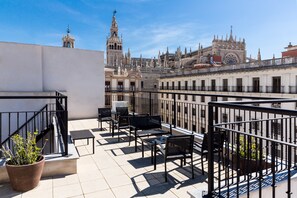Terraza en la azotea con mobiliario exterior, una planta en maceta y vistas a edificios históricos.