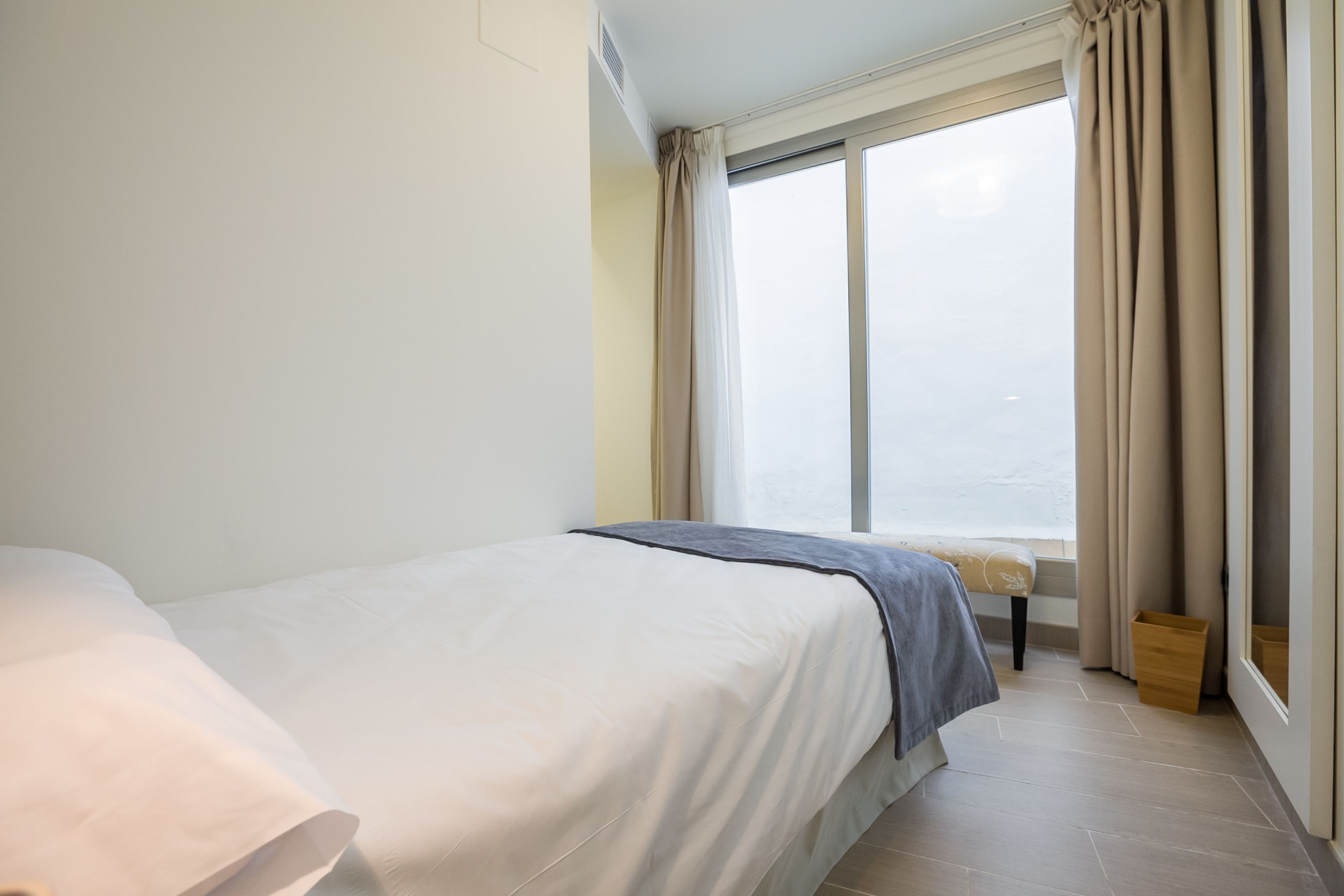 A bedroom with a bed, a window with curtains, and a small wooden bench.