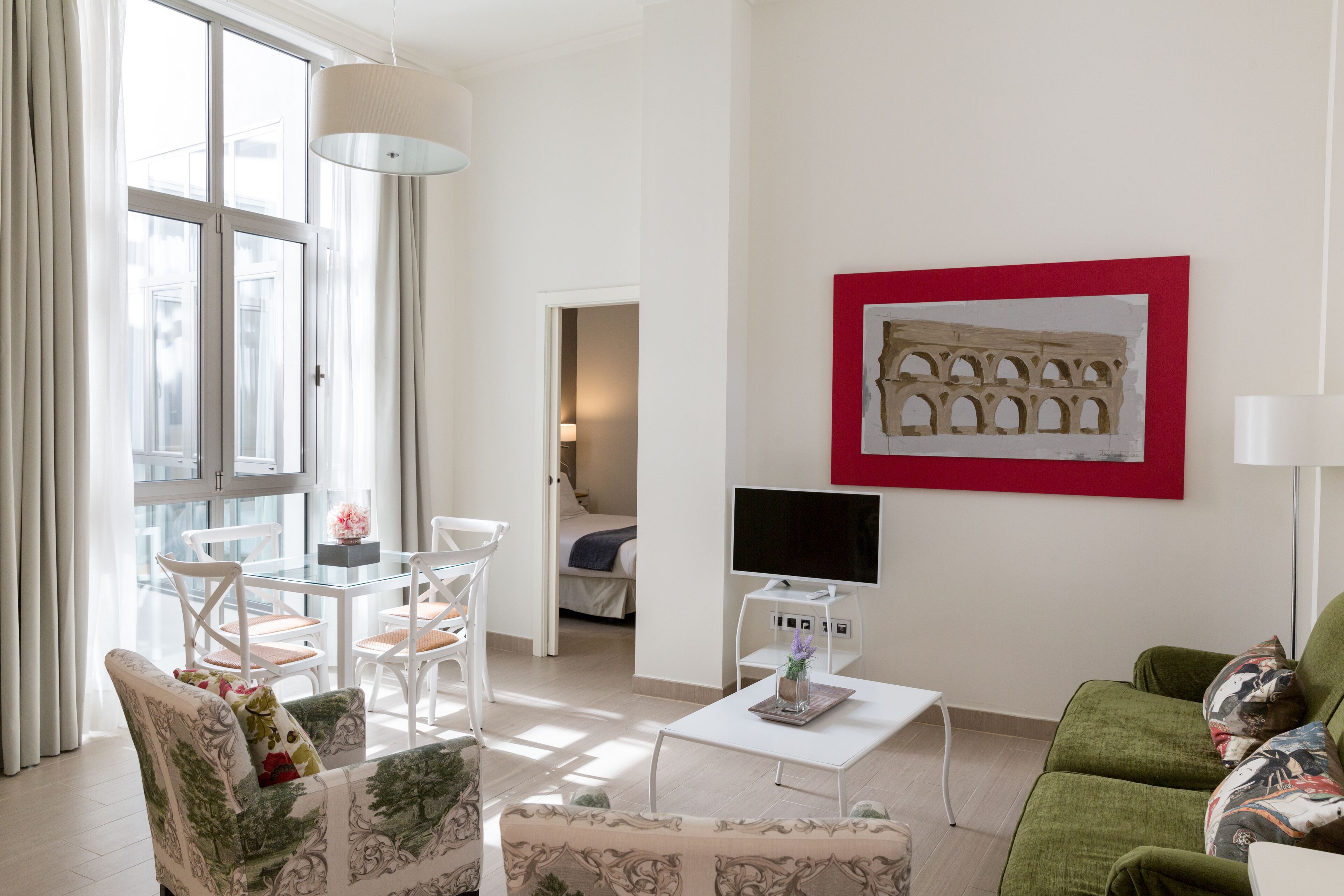 A modern living room with a glass dining table, white chairs, a green sofa, and a flat-screen TV.