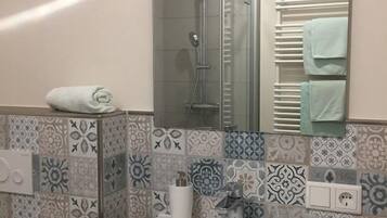 Een badkamer met patroontegels, een glazen douchecabine, een handdoekrek met opgevouwen handdoeken en een witte wasbak met een kraan.