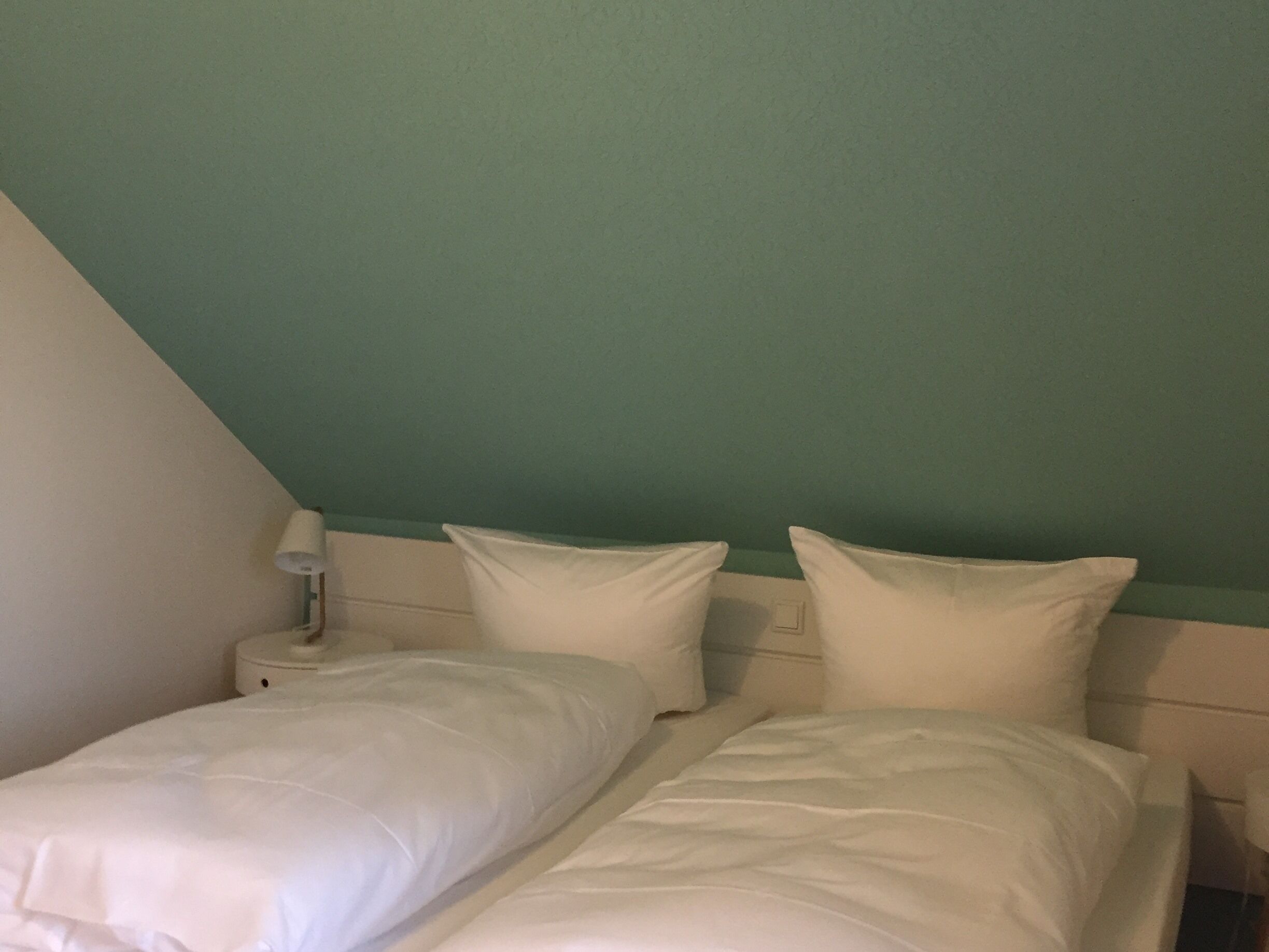 A twin bed with white bedding in a room with teal walls and a white nightstand.