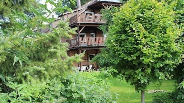A two-story wooden cabin with a balcony, surrounded by lush greenery. - Ferienhof Pankalla (Bassum)