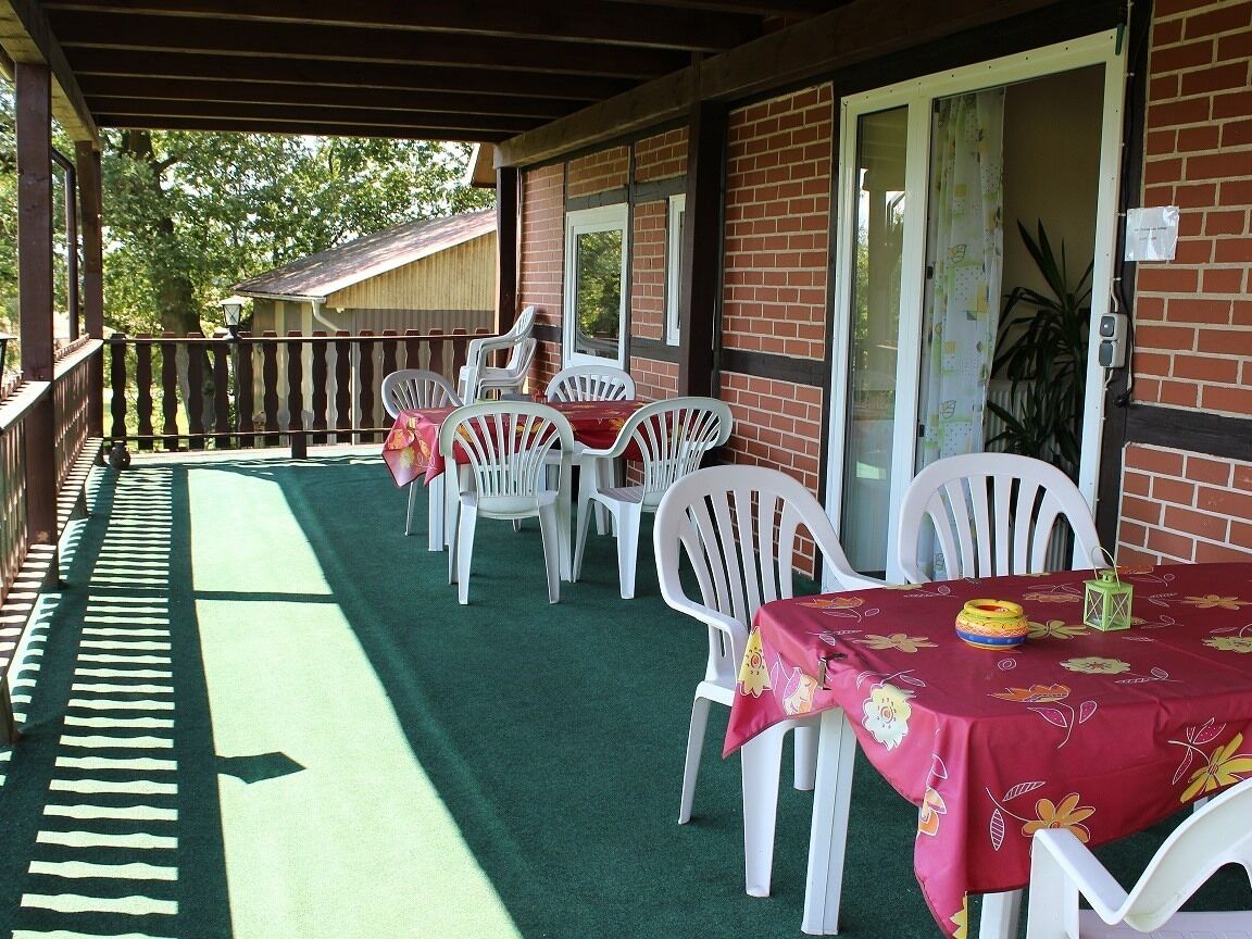 A covered outdoor area with a green carpet, white plastic chairs, and a table with a red tablecloth.