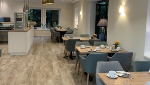 A modern dining area with wooden tables and chairs, pendant lighting, and a view of the outdoors. - Ferienhof Pankalla (Bassum)