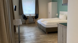 A hotel room with a bed, a desk with chairs, a wardrobe, and a window with curtains. - Ferienhof Pankalla (Bassum)