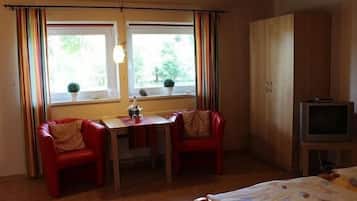 A room with a bed, a small table with chairs, a television, and windows with curtains.