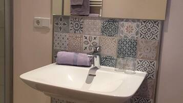 Un baño con un lavamanos blanco, un espejo y azulejos estampados en la pared.