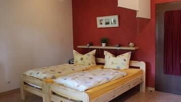 Una cama de madera en una habitación con paredes rojas, una estantería con objetos decorativos y una puerta con cortina.