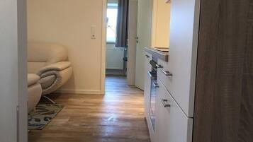 Un couloir étroit avec un canapé beige, un plancher en bois et une armoire blanche dotée de tiroirs.