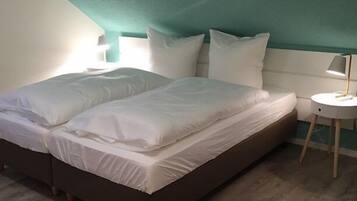 Una cama bien hecha con sábanas blancas en una habitación con paredes verde azulado y suelo de madera.