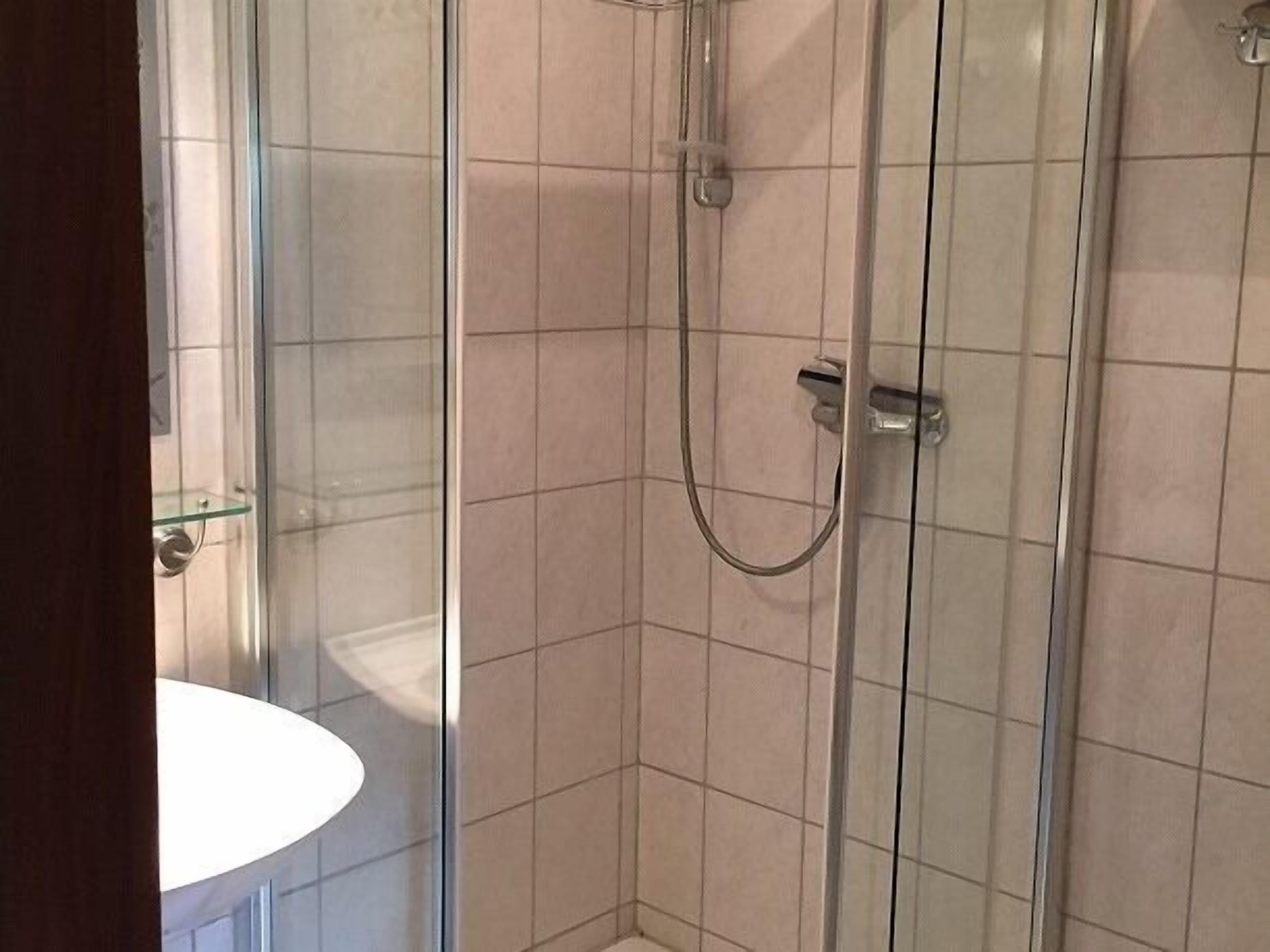 A bathroom with a glass shower enclosure, a white sink, and tiled walls.