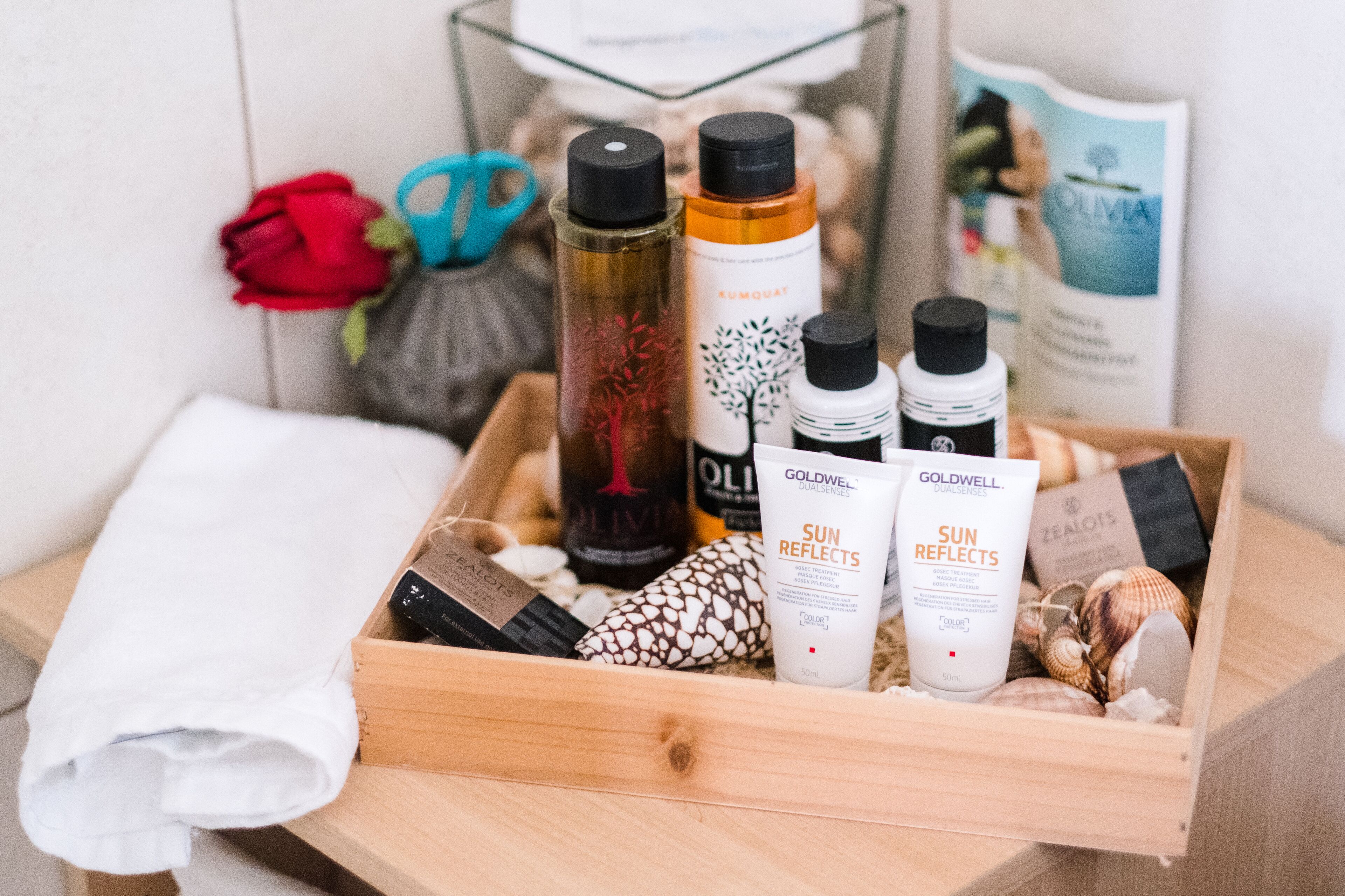 Un plateau en bois contenant divers produits de soins pour la peau, une rose rouge, des coquillages et une serviette blanche.