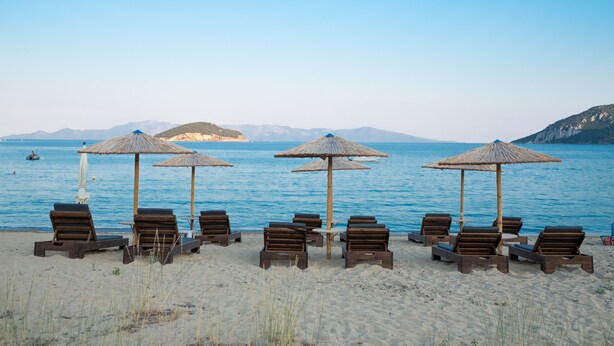 Ein Strand mit Holzliegen und Reetdachschirmen, die in Reihen zum Meer ausgerichtet sind.