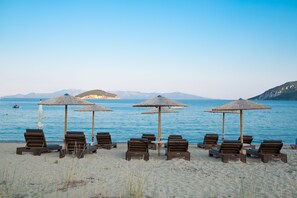 A beach with wooden lounge chairs and thatched umbrellas, arranged in rows facing the sea. - Blue Crystal Villa (Pangaio)