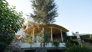 Ein modernes Haus mit überdachter Terrasse, Steinmauern und üppiger Bepflanzung.