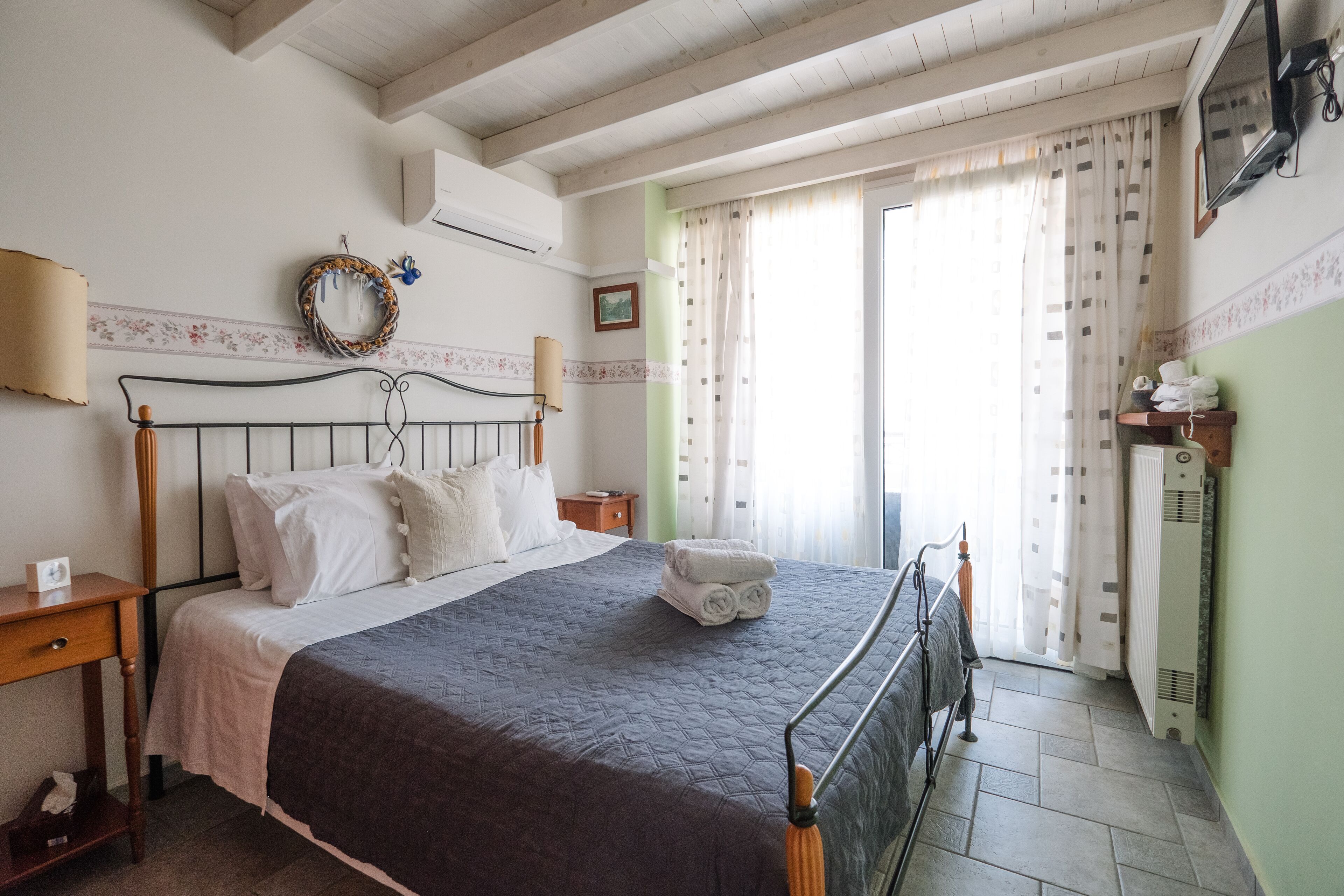 A bedroom with a bed, bedside tables, a wall-mounted TV, and a window with curtains.
