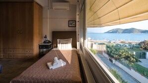 Ein Schlafzimmer mit Bett, Nachttisch, Kleiderschrank und Fenster mit Blick auf das Meer und eine entfernte Insel.
