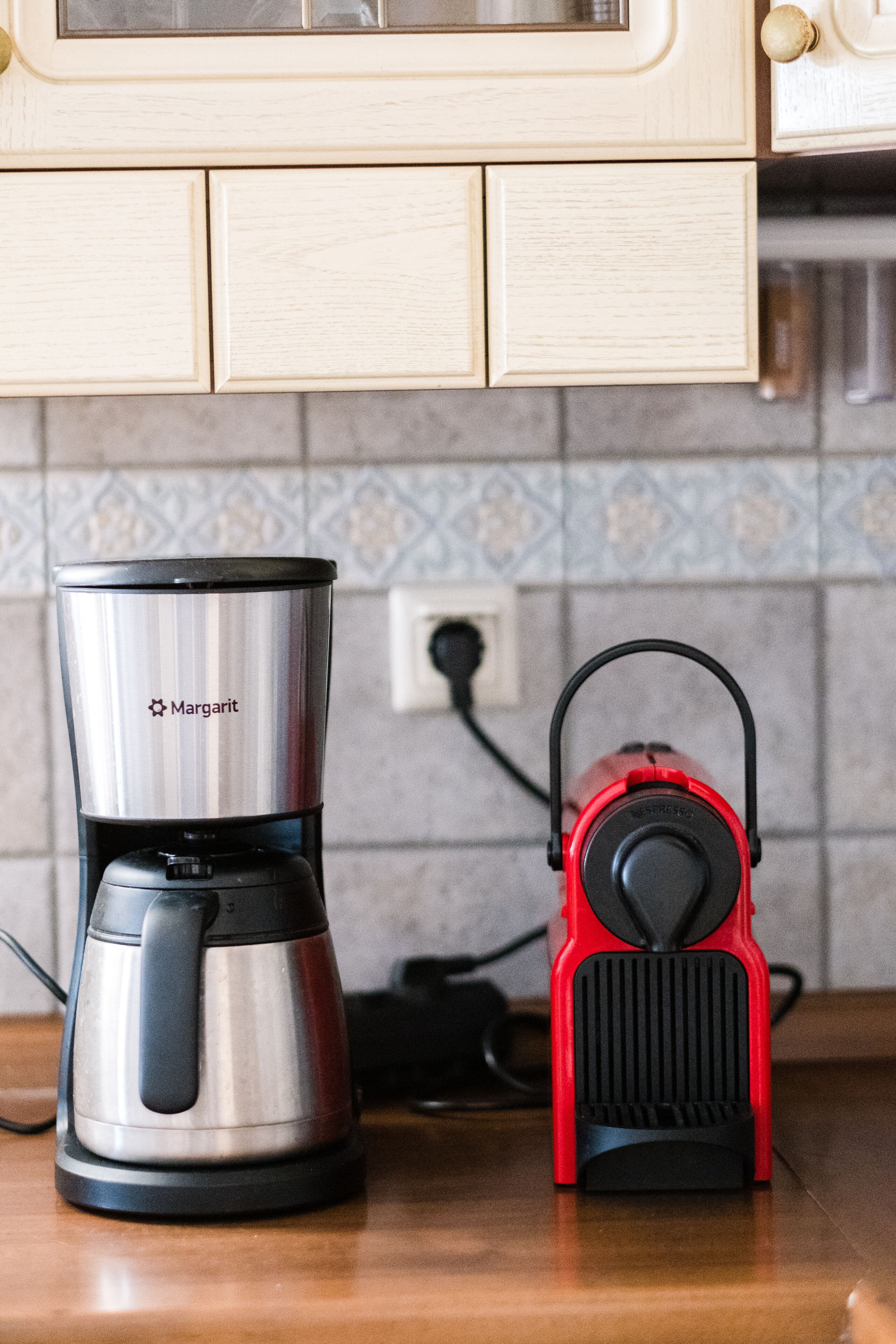 Een keuken met een roestvrijstalen koffiezetapparaat en een rode elektrische waterkoker op het aanrecht.