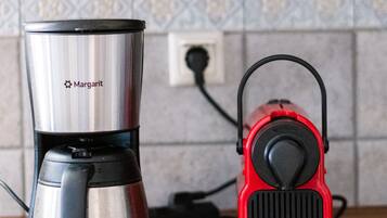Een keuken met een roestvrijstalen koffiezetapparaat en een rode elektrische waterkoker op het aanrecht.