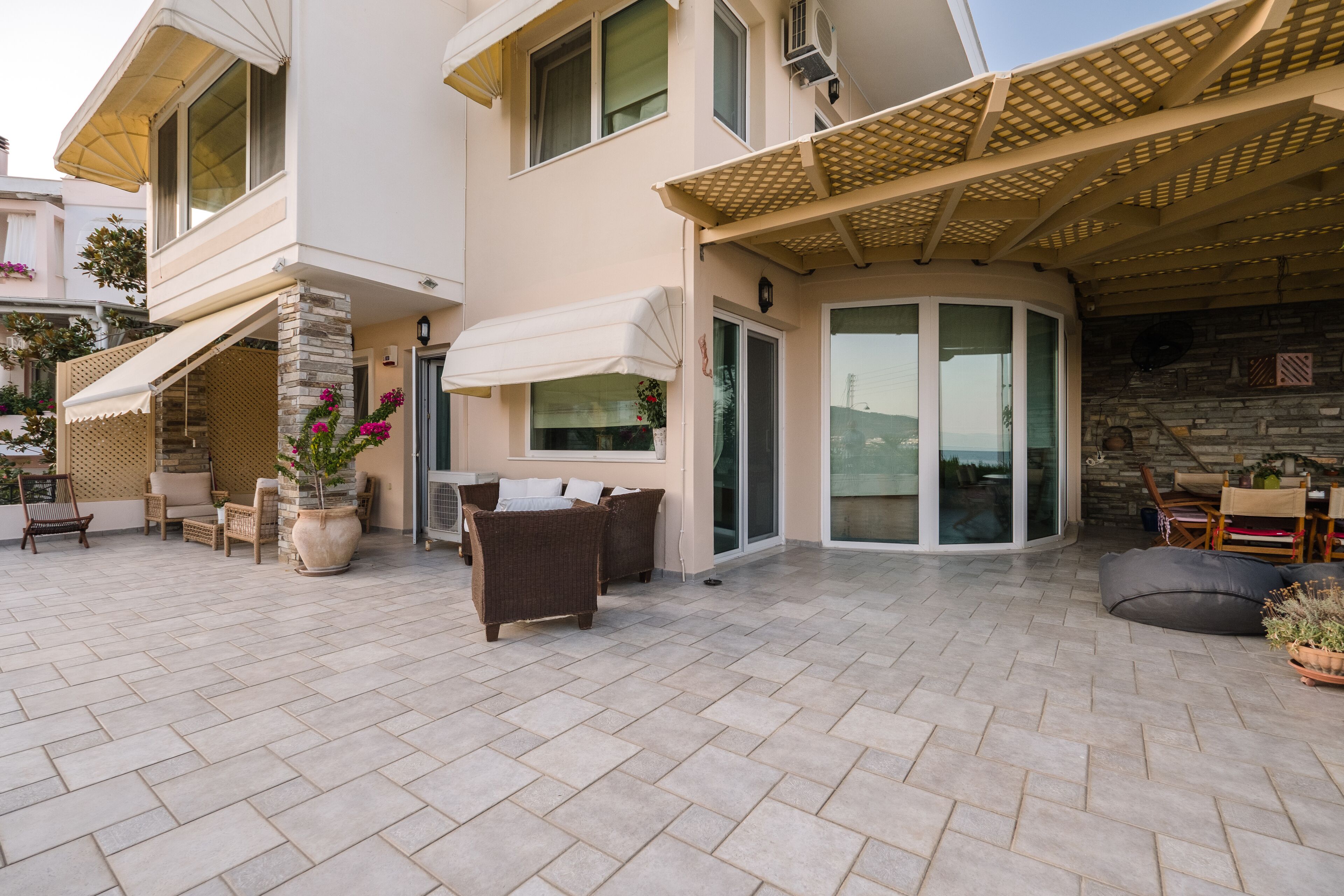 Una casa moderna con un patio que incluye mobiliario exterior, un área de estar cubierta y un muro de piedra.