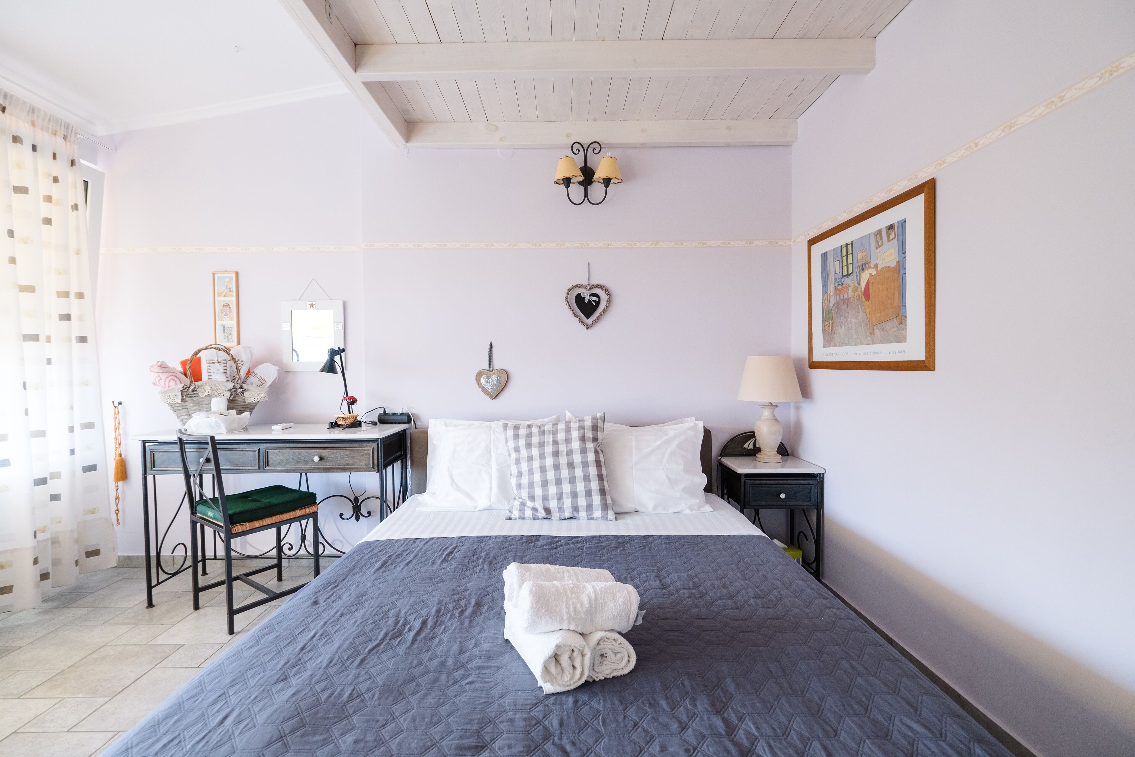 A neatly arranged bedroom with a bed, bedside table, desk, chair, and a wall-mounted lamp.