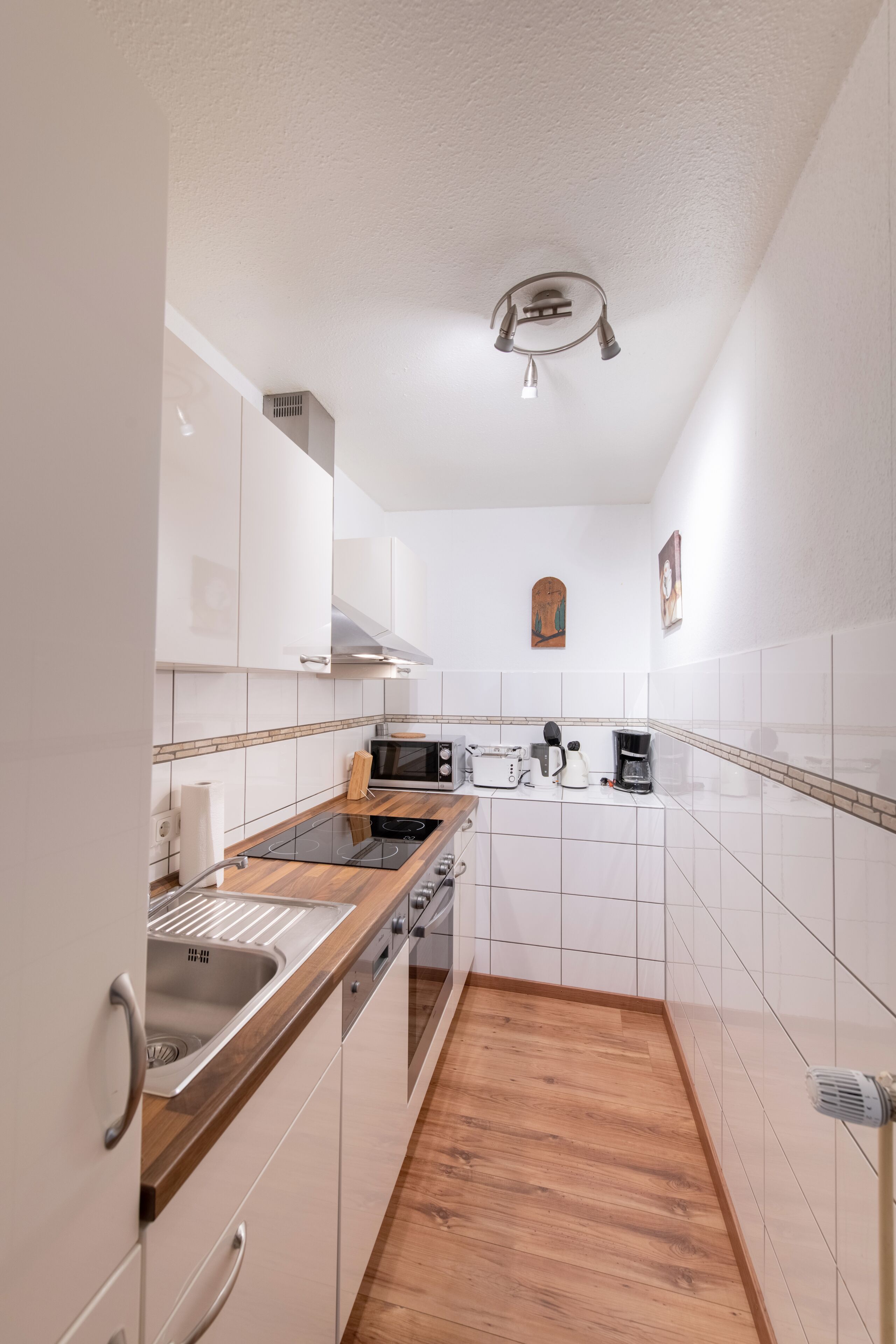 Une cuisine de taille réduite avec des meubles blancs, un plan de travail en bois et une cuisinière intégrée.