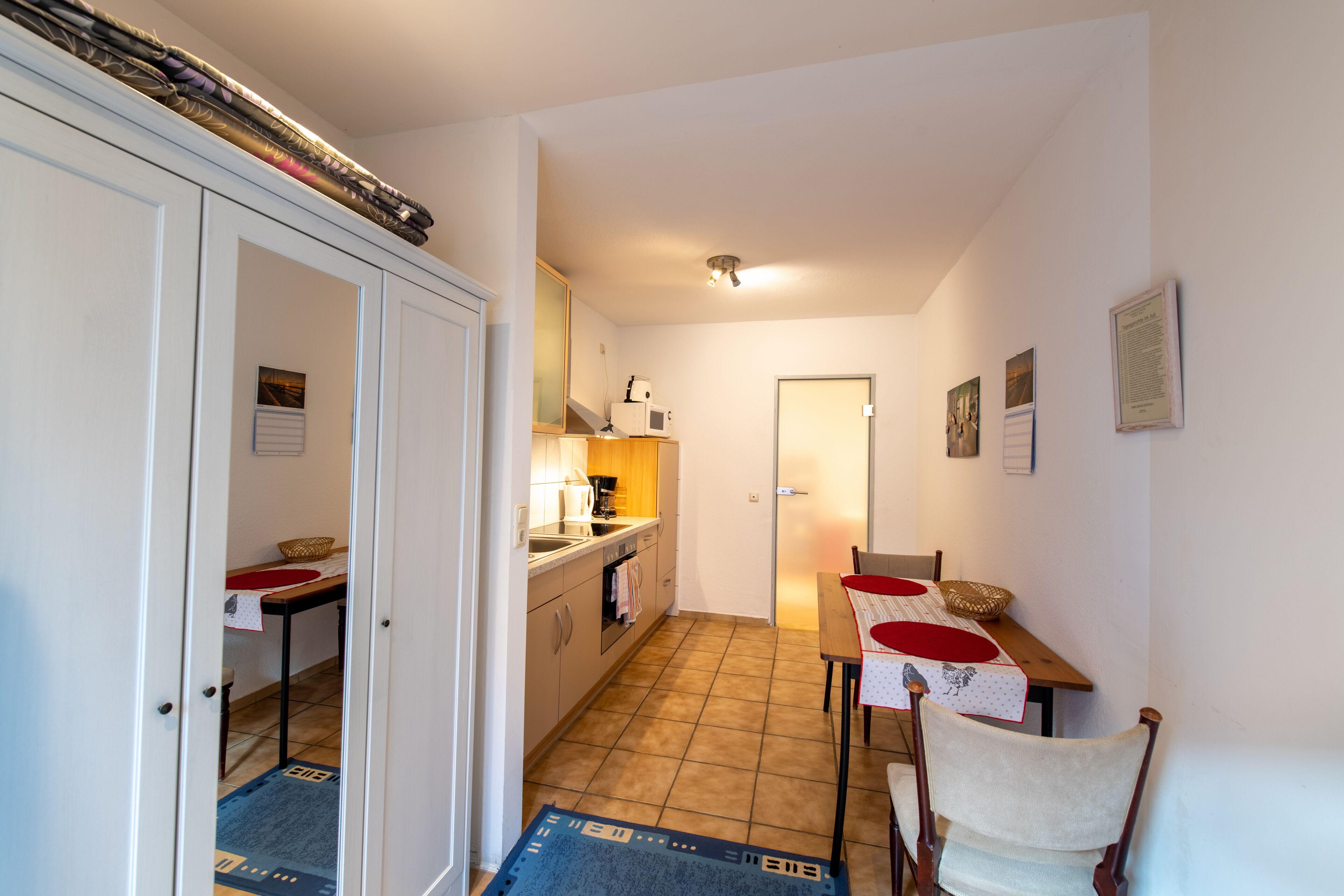 A compact kitchen with a dining area, featuring a tiled floor, white cabinetry, and a small table with chairs.