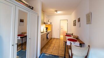 A compact kitchen with a dining area, featuring a tiled floor, white cabinetry, and a small table with chairs.