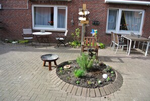 A patio area with a brick floor, a round table, and a wooden chair. There is a small garden bed with plants and flowers. - Ferienwohnung Kruppa (Ploen)
