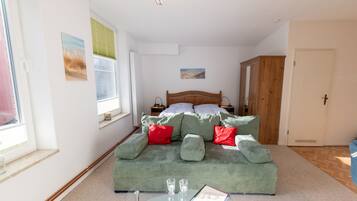 Un dormitorio con cama, sofá verde, una mesa de vidrio con controles remotos y una ventana con persianas.