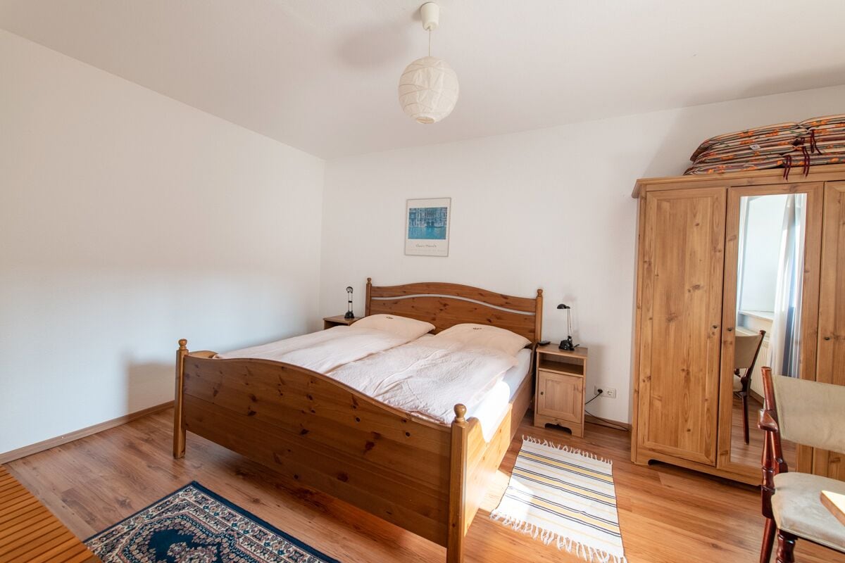 A bedroom with a wooden bed, a nightstand, a wardrobe, and a mirror.