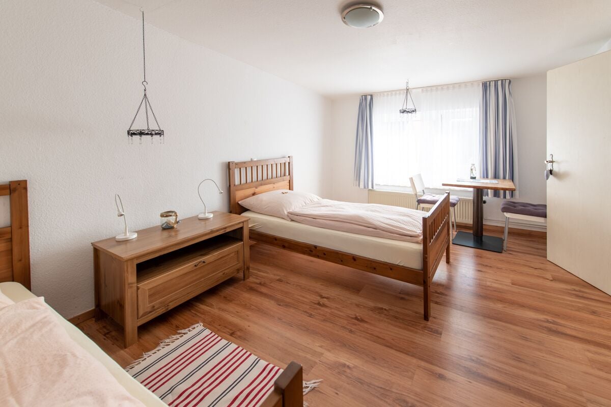 A bedroom with a wooden bed, a nightstand, a desk, and a chair.