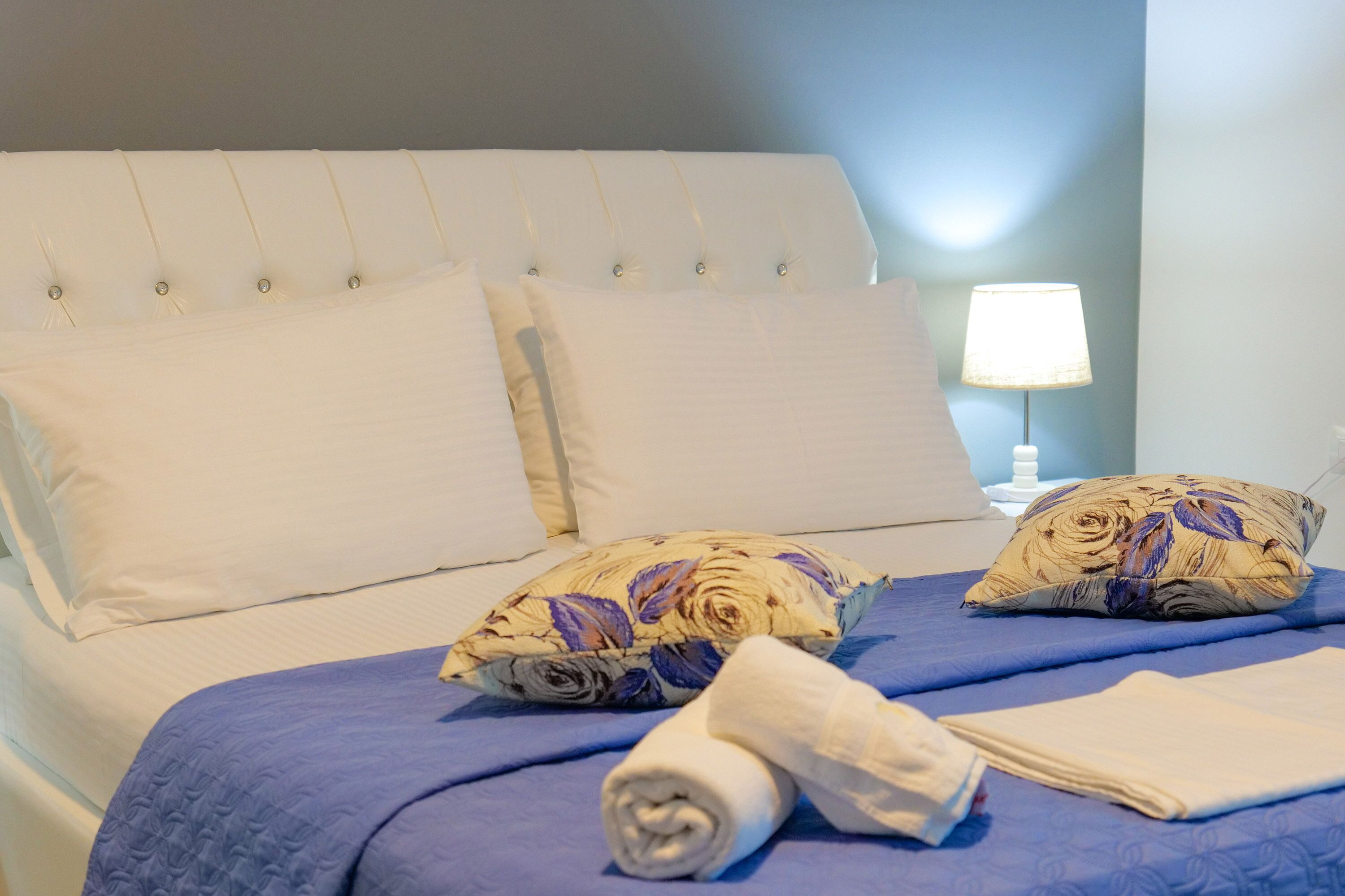 A neatly made bed with a blue bedspread, two decorative pillows, and a rolled towel.