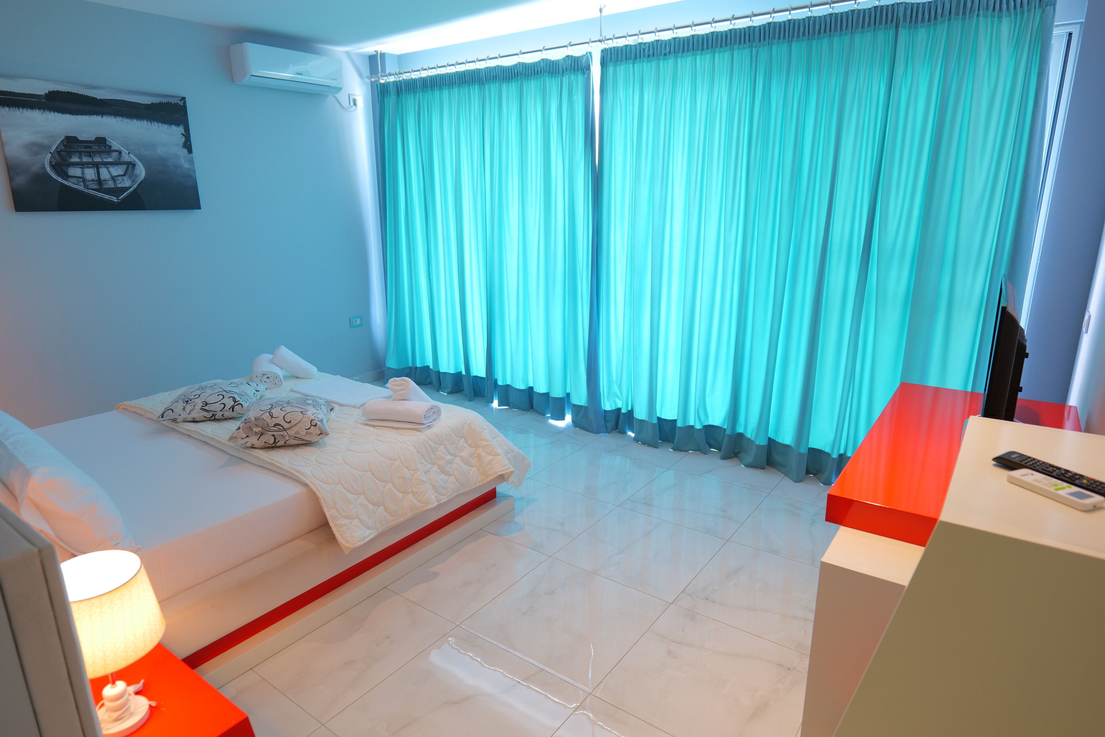 Una habitación de hotel moderna con una cama, una mesita de noche con lámpara, una ventana con cortinas y un cuadro en la pared.