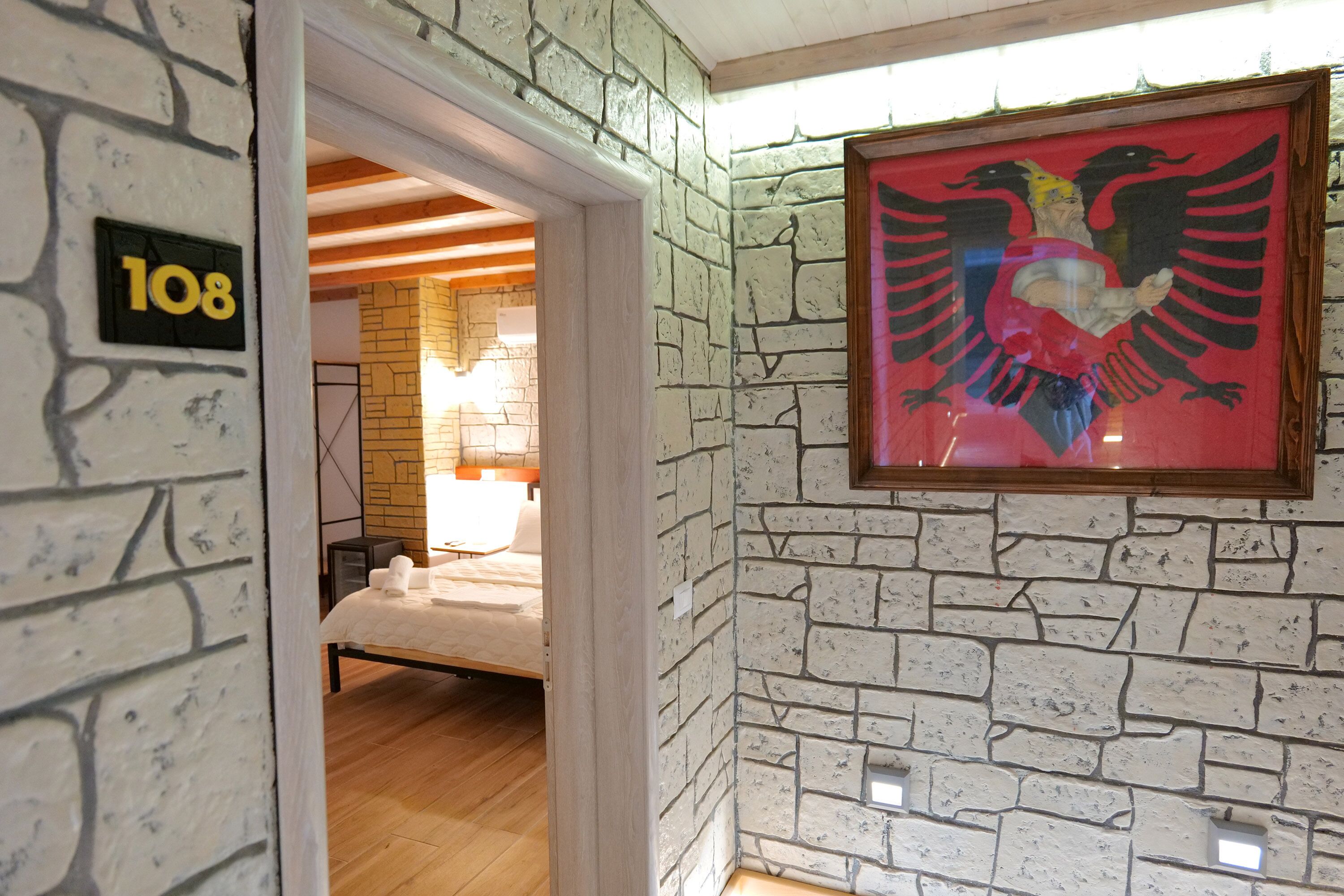 A room with a brick wall, a framed picture of an eagle, and a bed with white bedding.