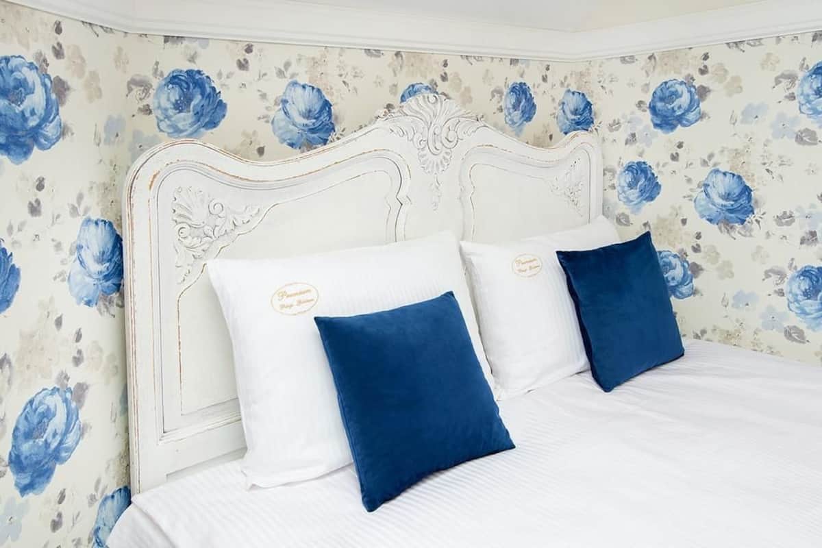 A bedroom with a white headboard, floral wallpaper, and two pillows.