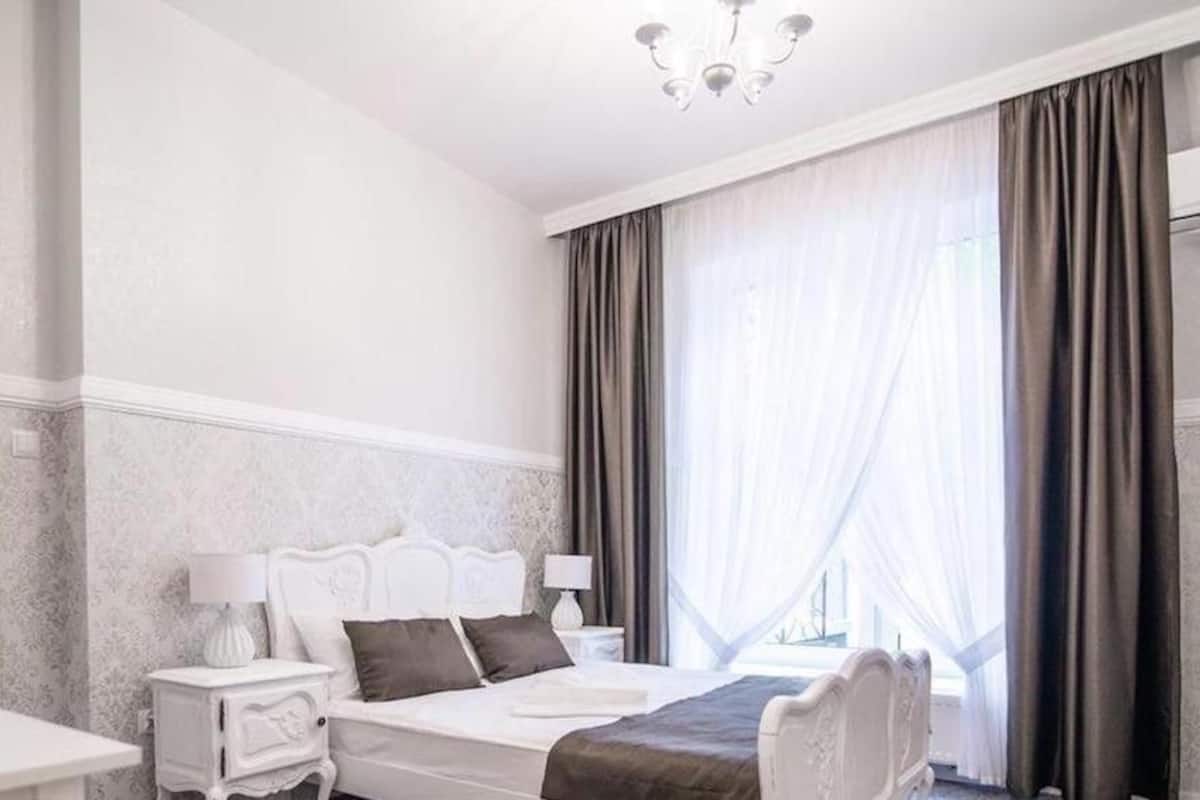 A hotel room with a bed, nightstands, a desk, and a large window with curtains.