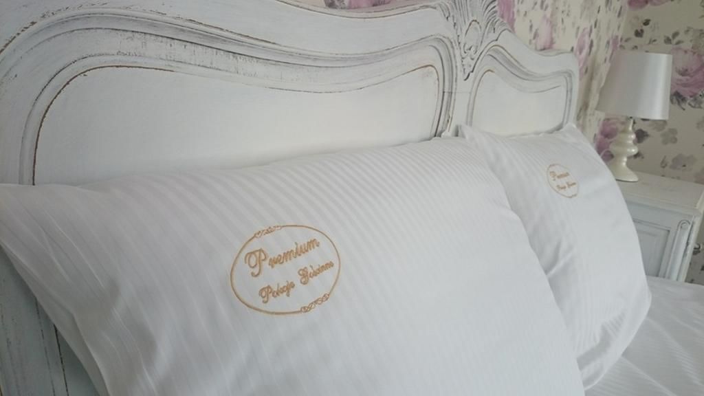 Een bed met witte lakens en een kussen met een goud geborduurd logo.