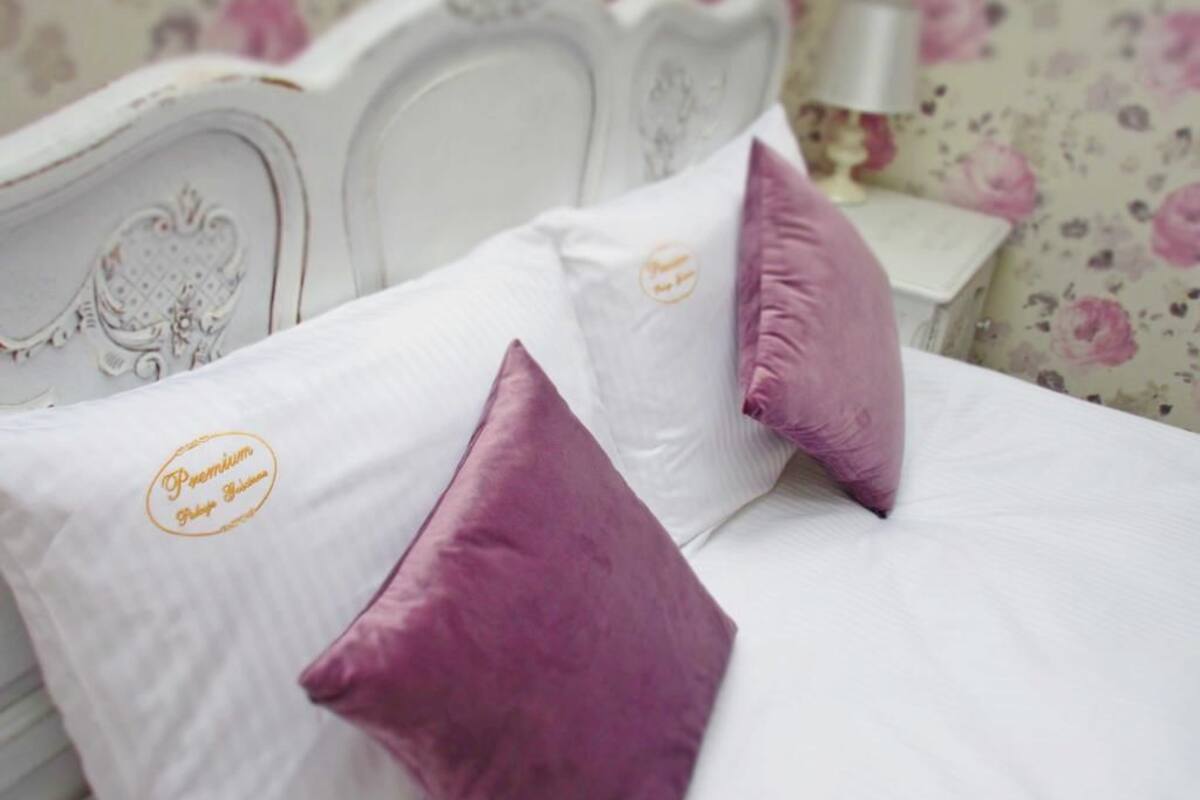 A bed with white bedding and two purple pillows, a floral wallpaper background, and a white headboard.