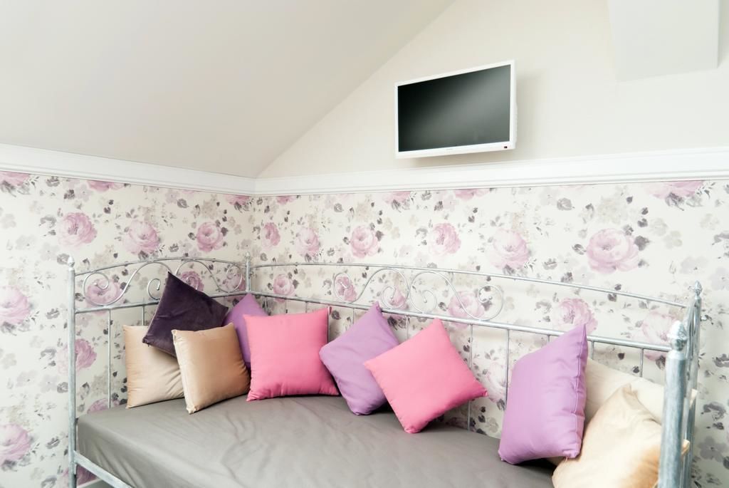 Une chambre d’angle avec un lit en métal, un papier peint à motifs floraux et un téléviseur fixé au mur.