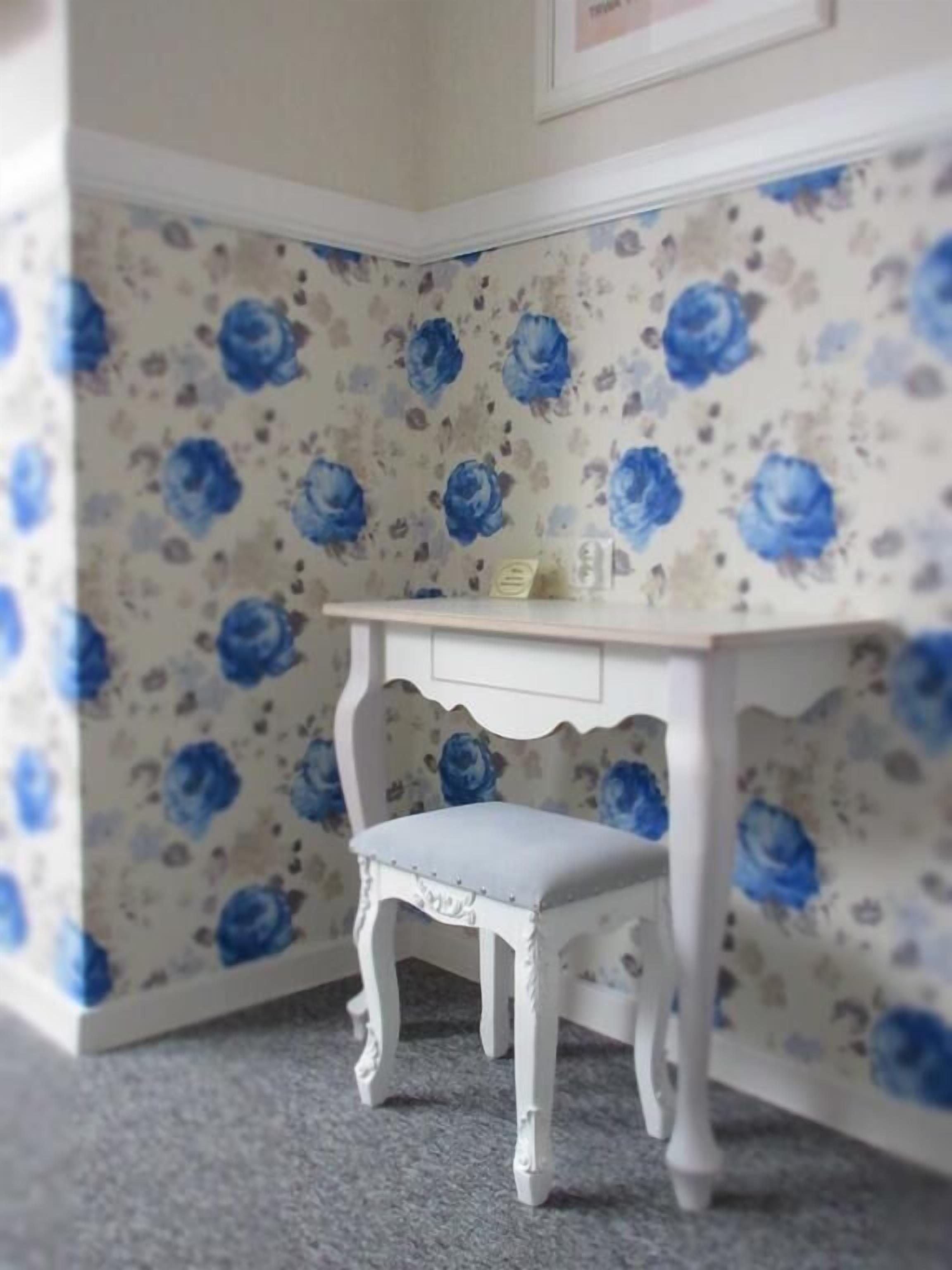 A corner room with a small white desk and chair against a floral wallpaper.